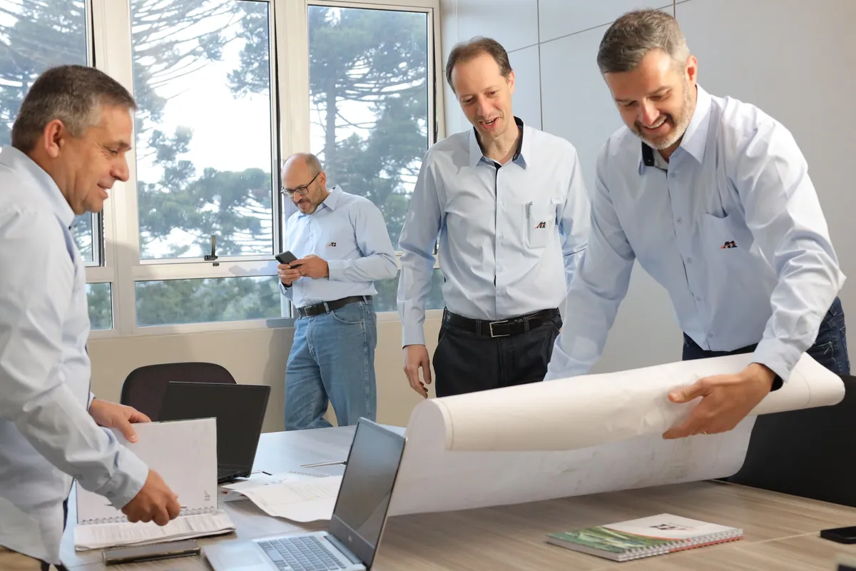 Engenheiros em pé analisando plantas impressas sobre a mesa de reunião