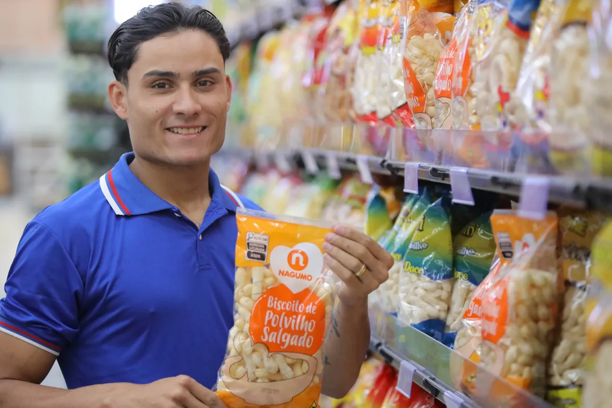 Colaborador do Nagumo sorri segurando um produto no corredor da loja