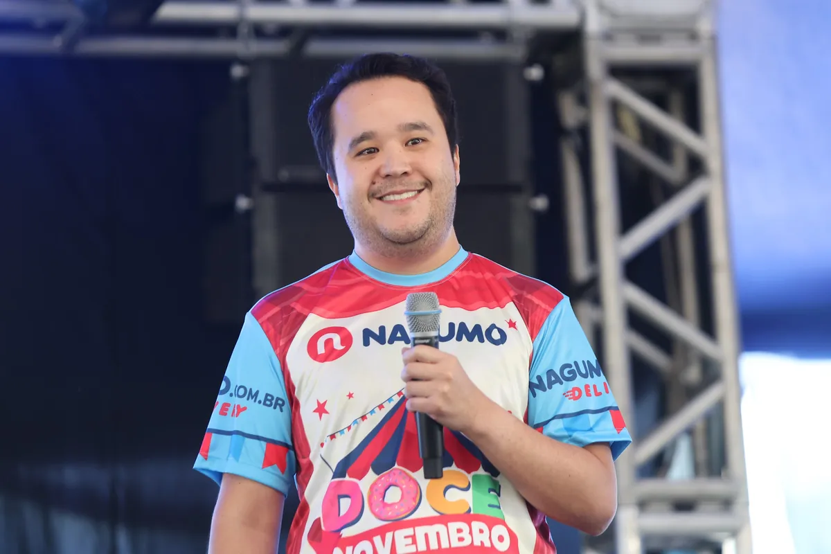 Apresentador sorri com microfone no palco do evento Doce Novembro do Nagumo