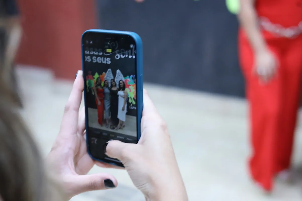 Mãos segurando um celular que fotografa formandas em evento da UniPiaget